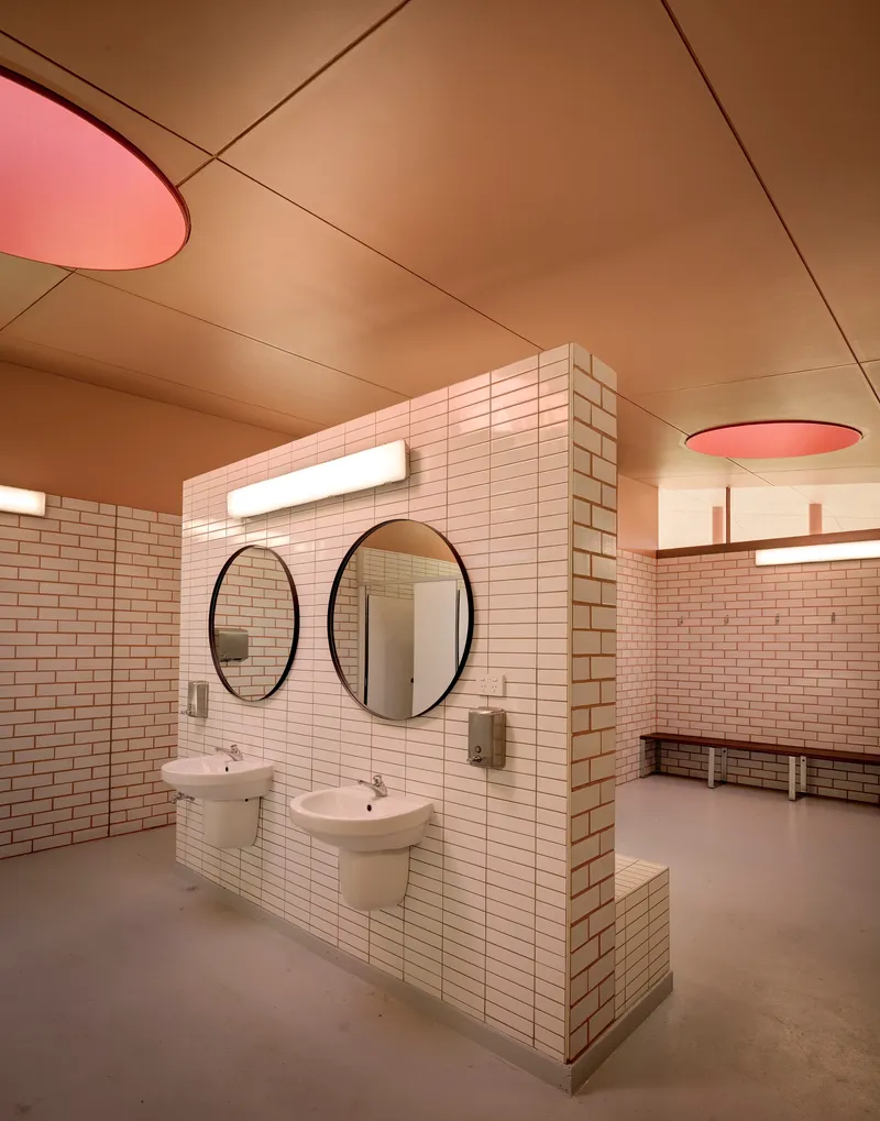 Freestanding tiled washbasin wall with round mirrors beneath pink ceiling light fixtures