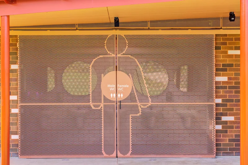 Perforated metal screen with restroom signage silhouette mounted in front of brick wall
