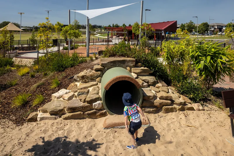 Concrete tunnel entrance surrounded by stacked sandstone boulders and native planting with a child approaching