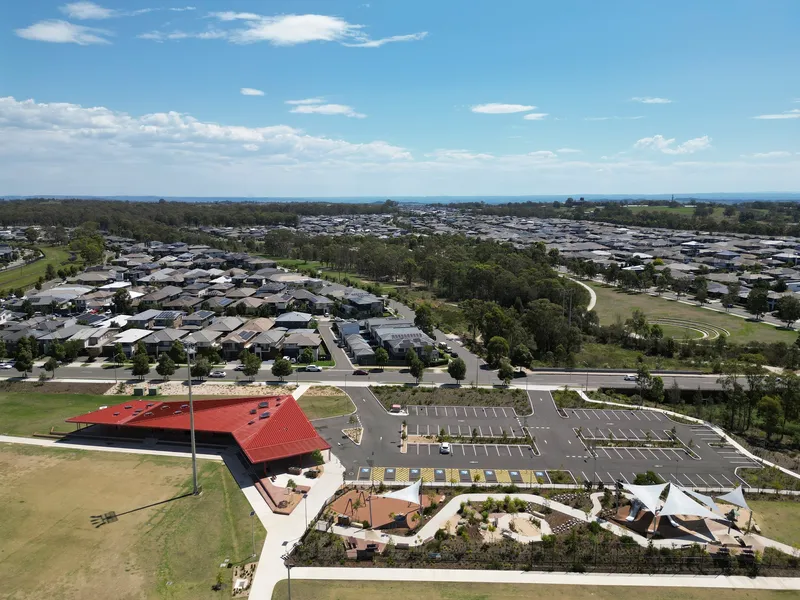 Aerial view of the red-roofed pavilion and parking area surrounded by playing fields and suburban housing