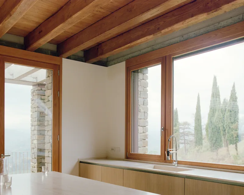 Kitchen counter with timber base units below windows framing cypress trees in misty landscape beyond
