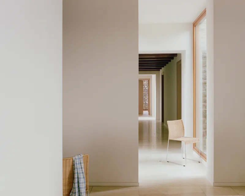 Corridor view through white walls and doorways revealing stone column and wicker chair in daylight