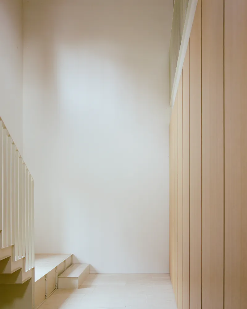 Stairwell with pale stone steps ascending past vertical wood paneling and white plaster walls