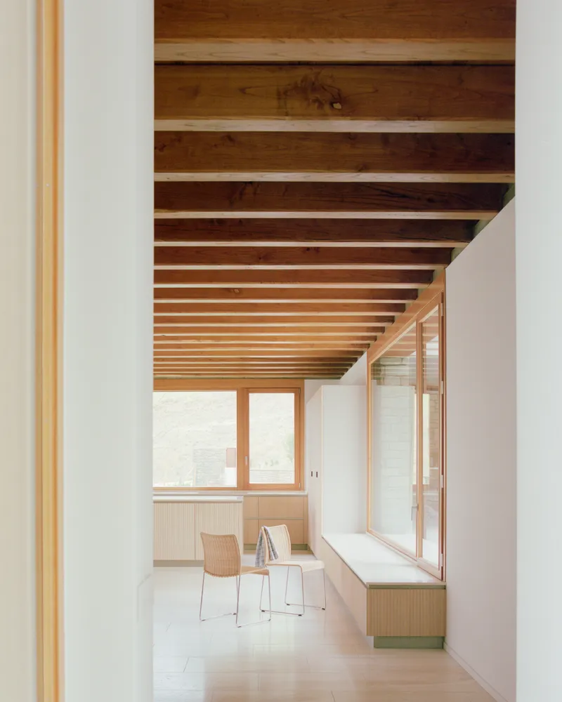 Interior hallway with exposed timber ceiling beams and a window bench in soft daylight