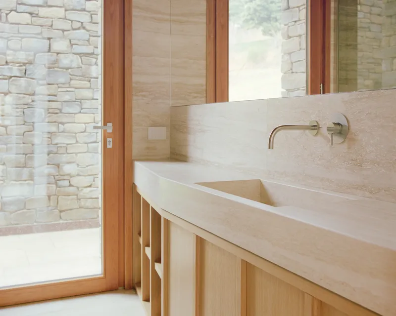 Bathroom vanity in pale stone with integrated sink and timber cabinetry beside stacked stone wall