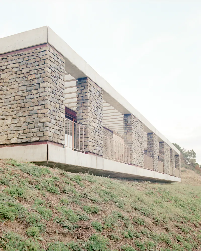 Side view of the elevated structure with stacked stone columns and concrete soffit above sloping terrain