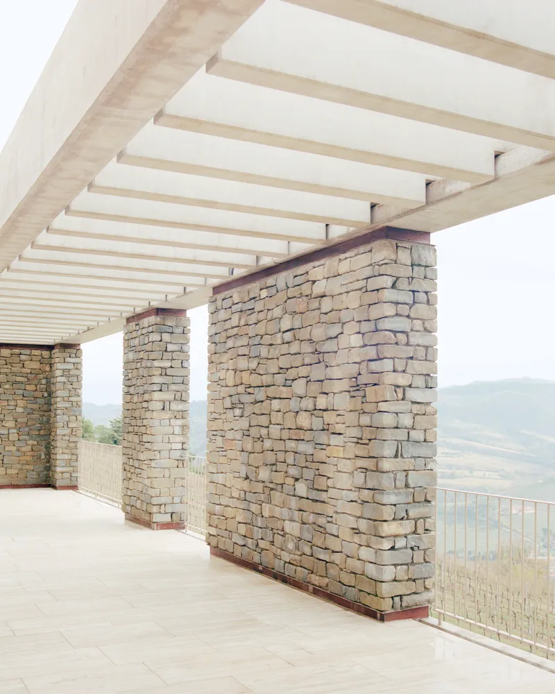 Covered terrace showing handlaid stone piers supporting timber beam and joist roof structure in hazy light