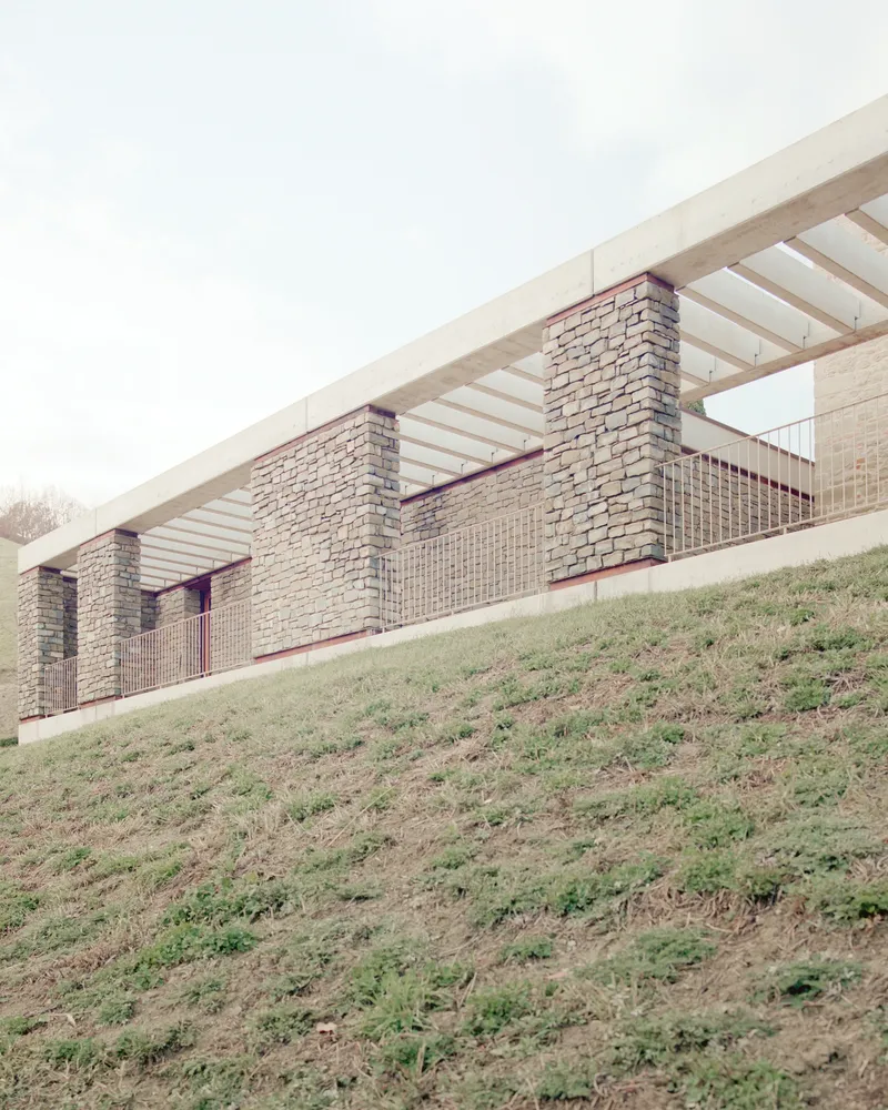 Brick facade with timber slatted roof canopy rising above a grassy hillside
