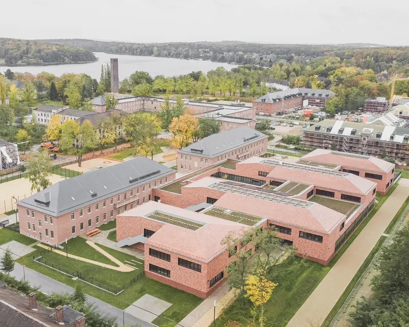 Aerial view of pink brick buildings with green roof terraces arranged around a central courtyard near a lake