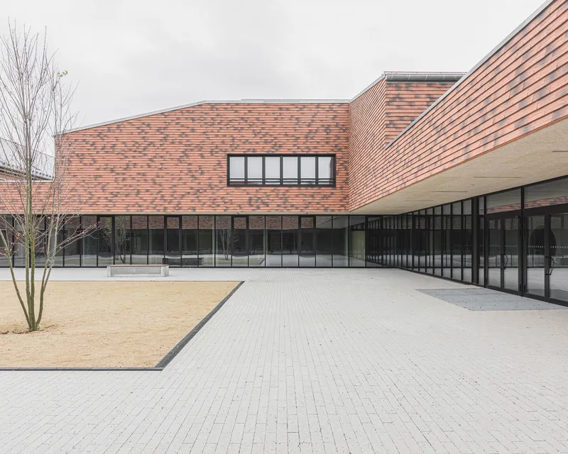 Paved courtyard with gravel bed and bare trees beneath pink brick facades and black-framed glazing