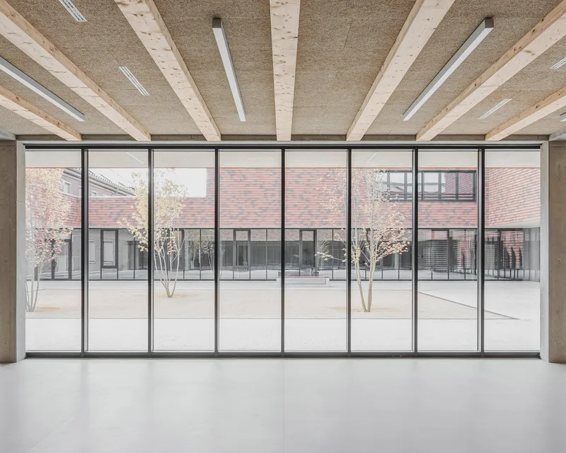 Interior gallery with timber ceiling beams overlooking a courtyard through floor-to-ceiling steel-framed glazing