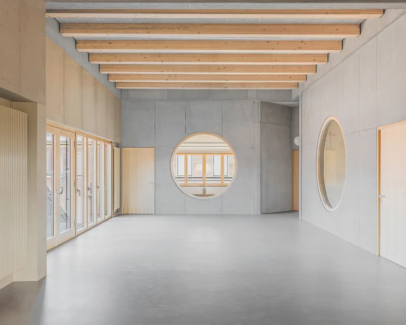 Corridor with exposed timber joists above concrete walls featuring two circular windows with timber reveals