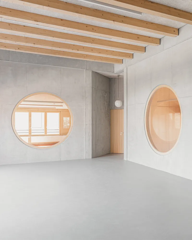 Polished concrete floor beneath exposed timber beams with circular windows framing adjacent rooms