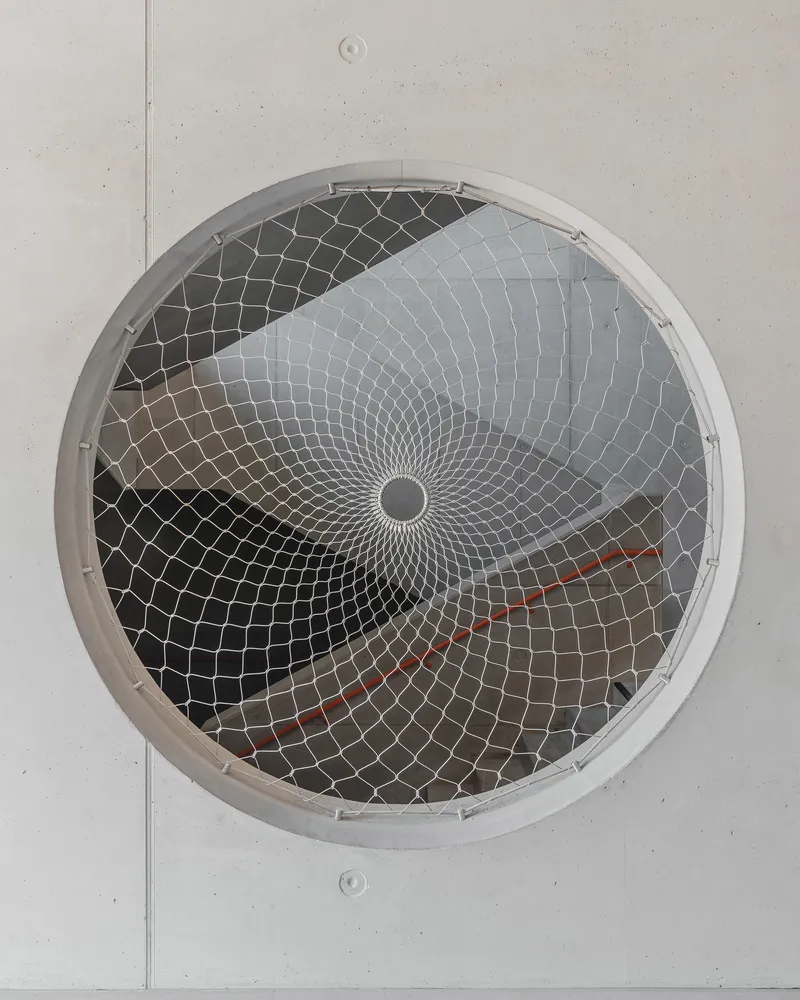 Circular ceiling vent with spiraling metal mesh guard in a light grey panel