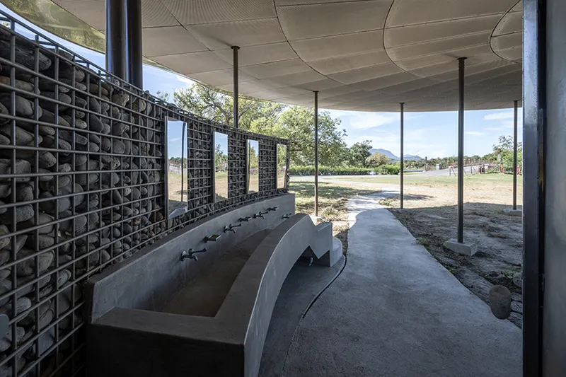 Interior space with gabion stone walls and concrete basin beneath the paneled ceiling and steel columns