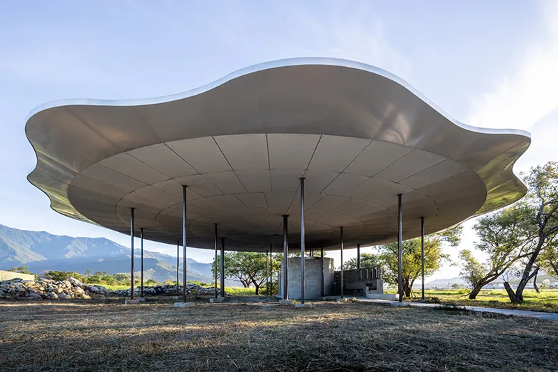 Undulating canopy roof supported by slender black columns with mountains and trees in the background