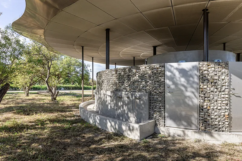 Concrete service core with gabion basket screens and metal door under the paneled canopy