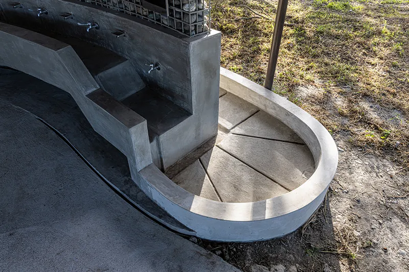 Concrete water basin with stepped trough and gabion wall in dappled sunlight
