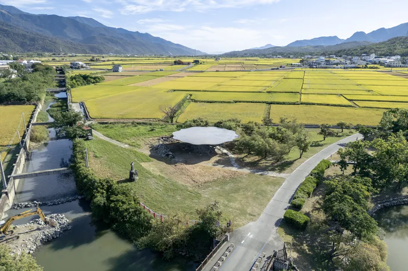 Aerial view of a circular roof structure set among rice paddies with mountains in the distance
