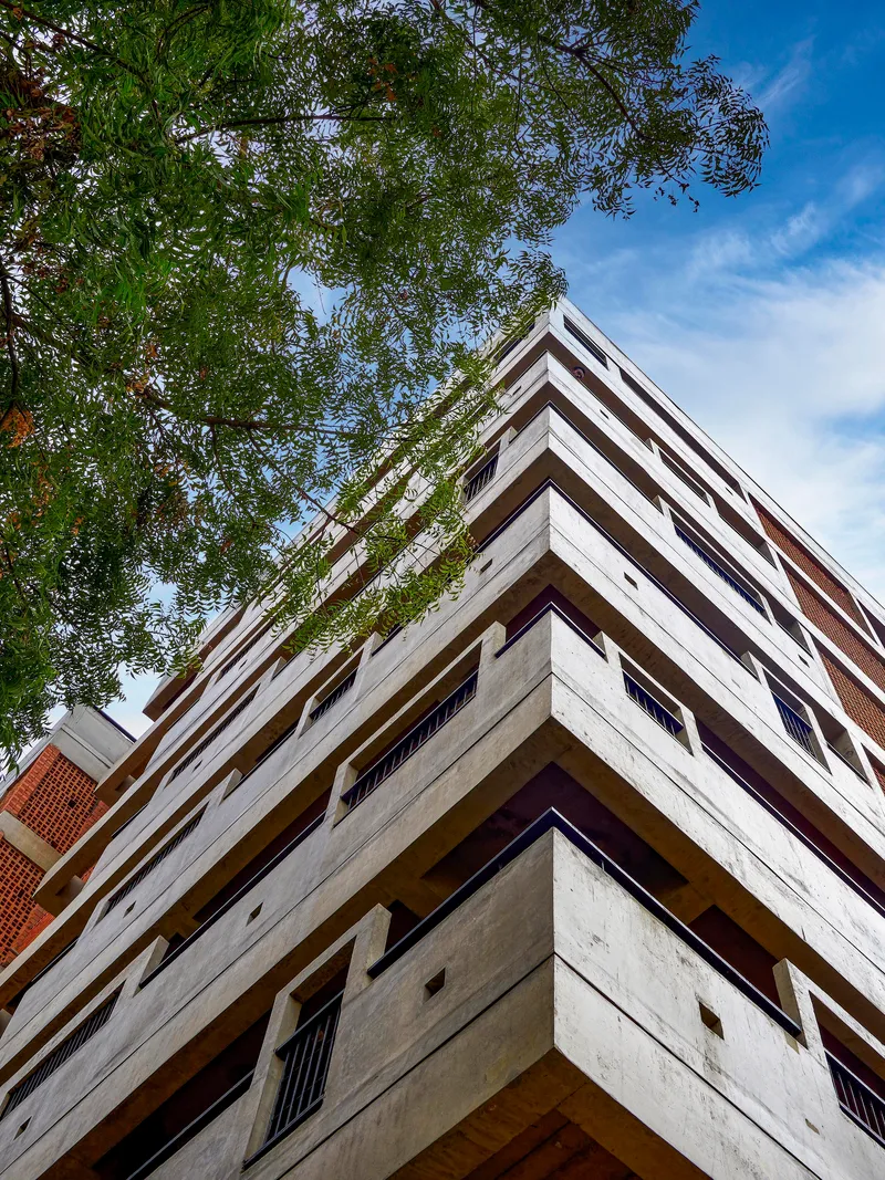 Upward view of the stacked concrete balconies with recessed openings framed by overhanging tree branches