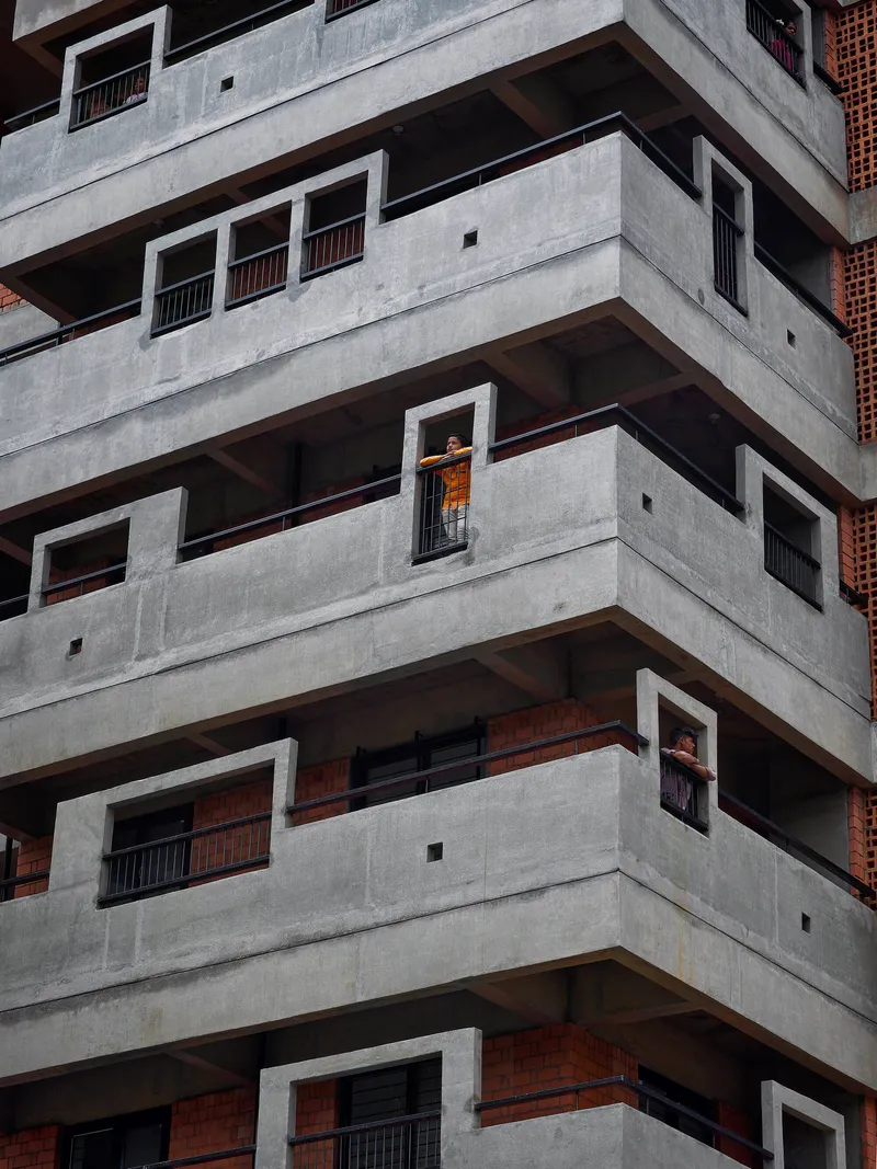 Stacked concrete balconies with deep recesses and a resident visible in one window opening