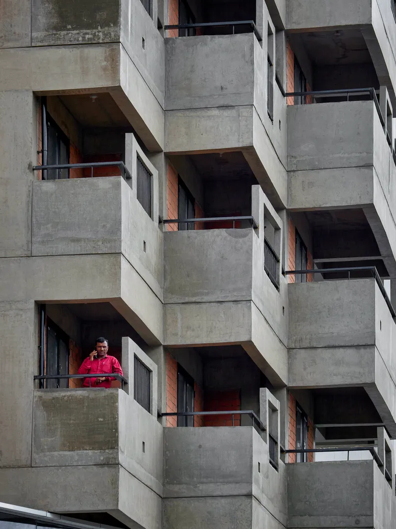 Concrete balconies with metal railings and exposed brick walls where a resident in red stands looking out