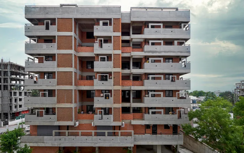 Multistory residential facade with concrete balconies and terracotta brick screens under a cloudy sky