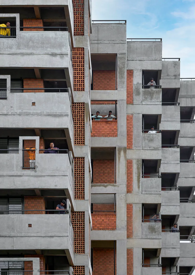 Staggered concrete balconies with exposed brick infill and residents visible in the window openings