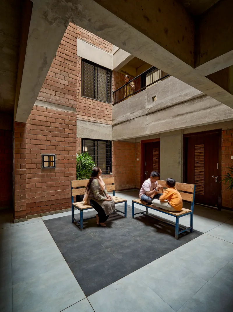 Interior courtyard with terracotta brick wall, skylight opening, and residents seated on benches below