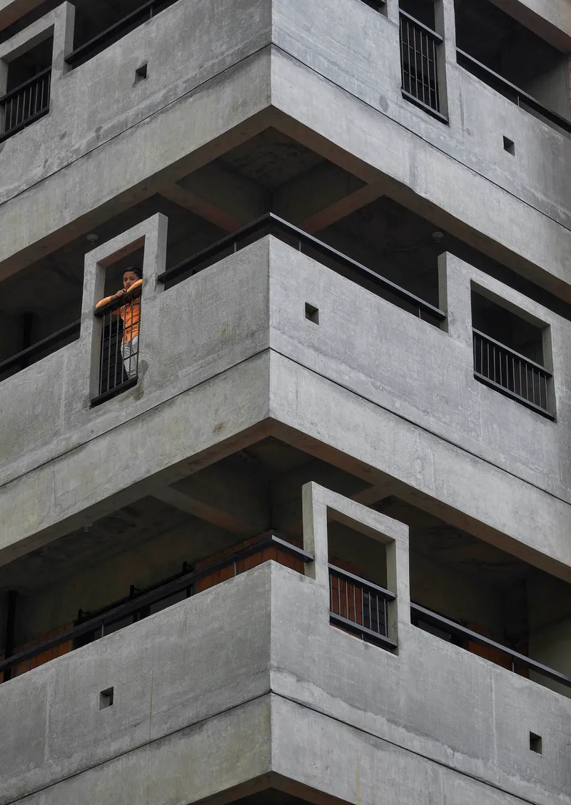 Corner detail of stacked concrete balconies with deep recesses and a resident in the window