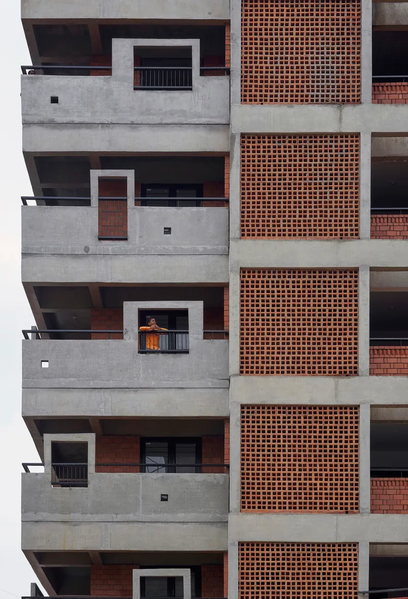 Stacked concrete balconies with terracotta brick panels where one resident leans on a railing