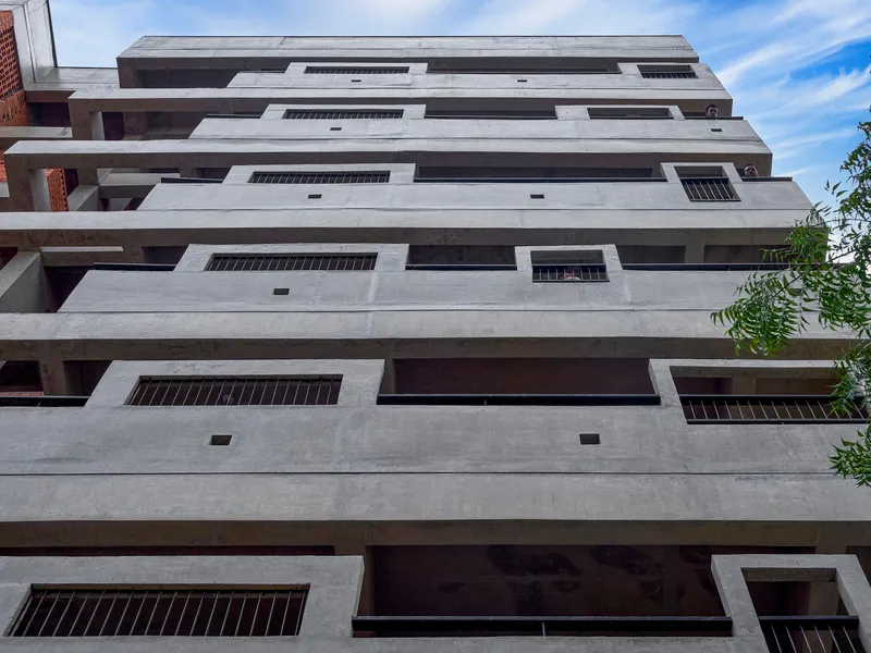 Ground-up view of the stepped concrete facade with deep balconies under a bright blue sky