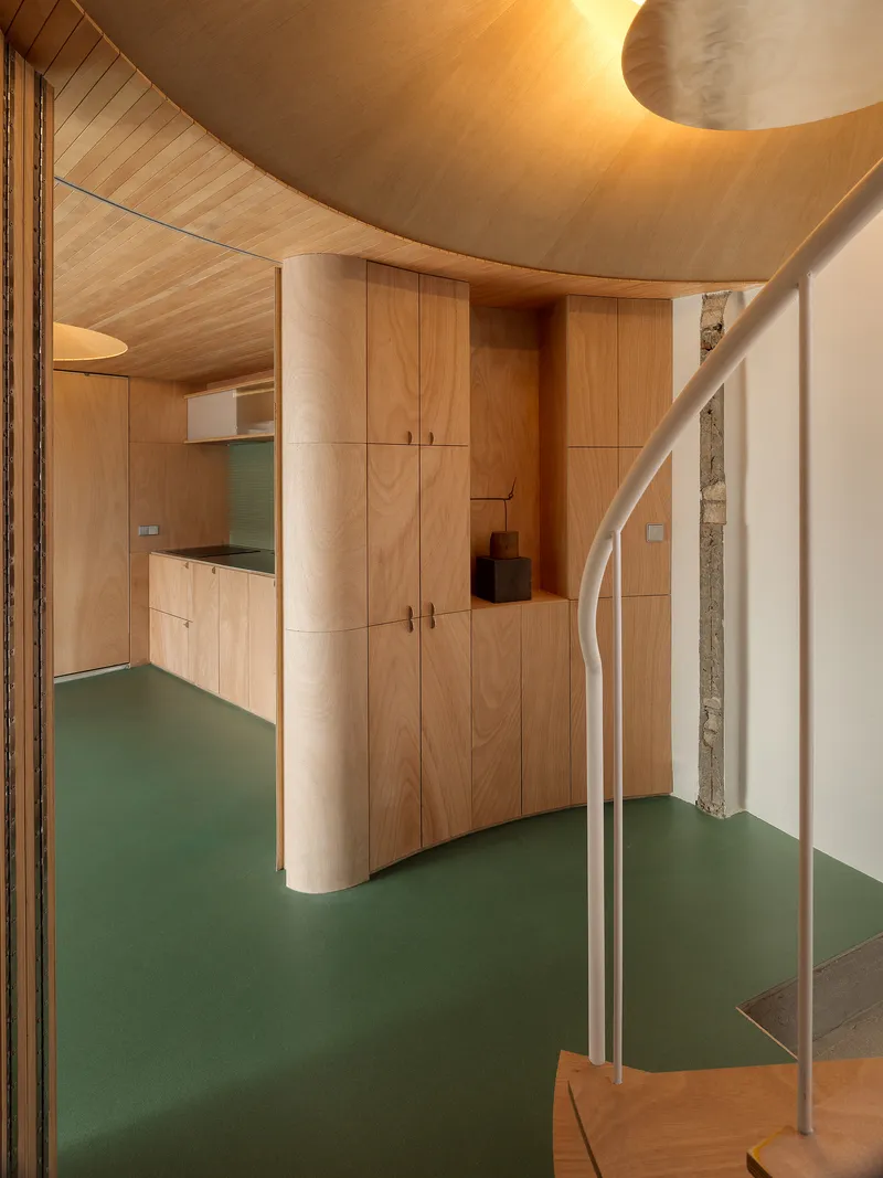 Curved timber-clad column and built-in cabinetry with spiral stair under warm indirect lighting