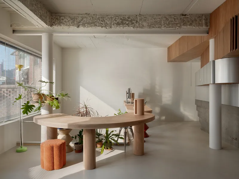 Workspace with sculptural timber table and potted plants in afternoon sunlight beneath exposed concrete beam