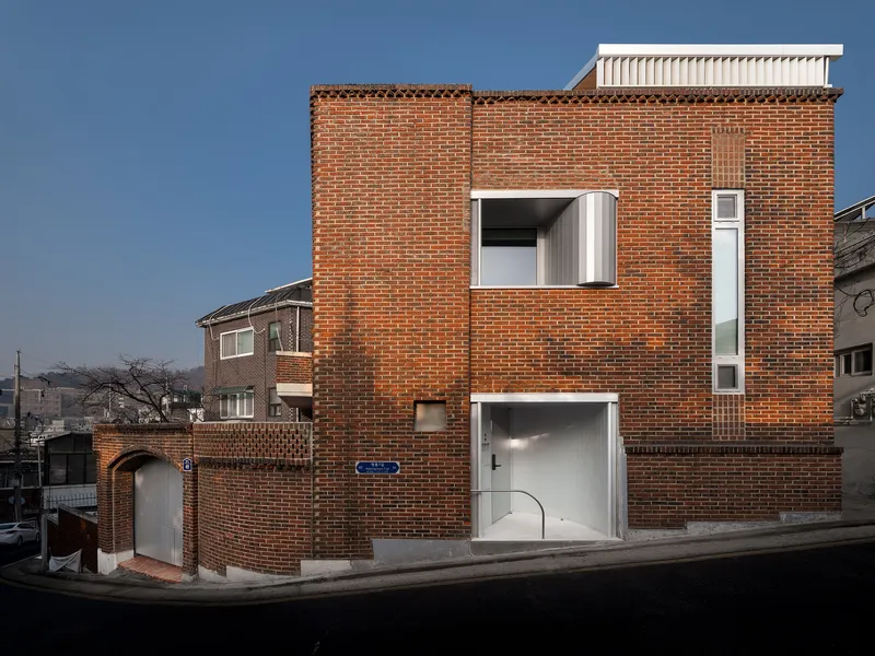 Red brick facade with white metal window inserts and rooftop addition under a clear blue sky