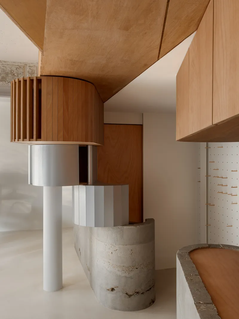 Detail of the curved timber kitchen hood with steel range, white supports, and concrete cylinder below plywood cabinetry
