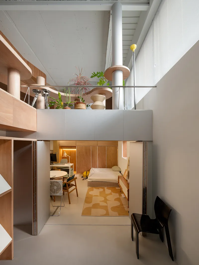 View into sleeping nook beneath mezzanine with patterned rug and timber wall panels in warm lighting
