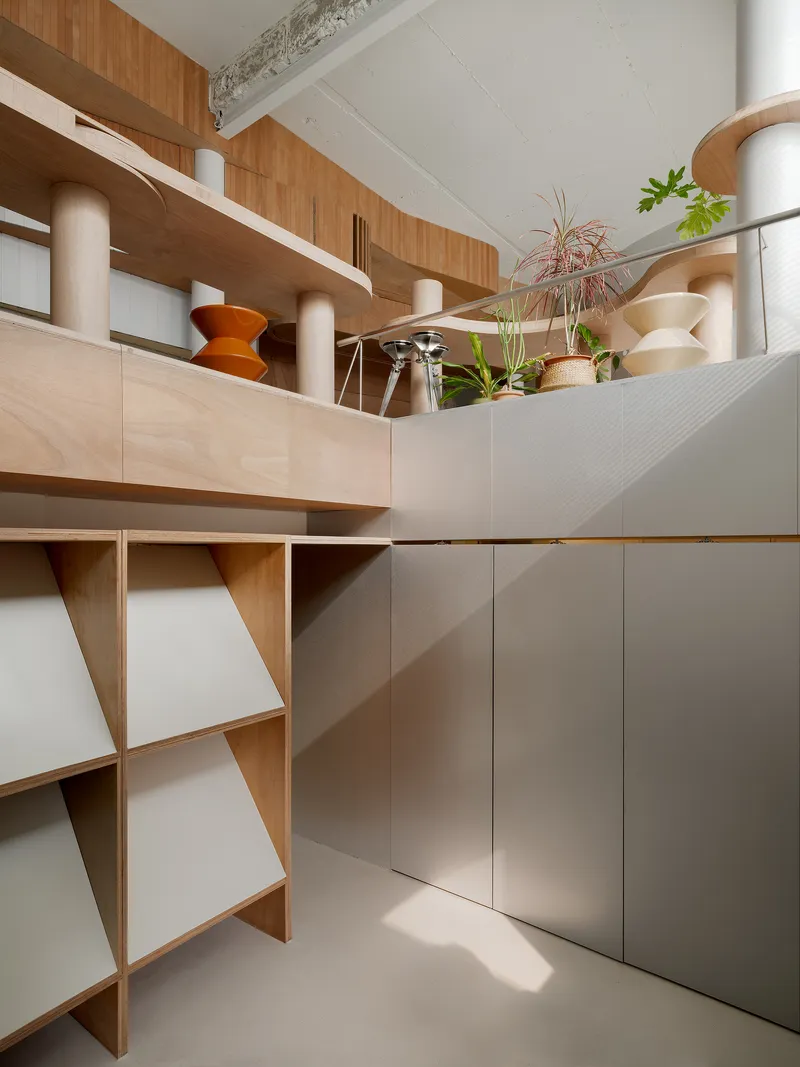 Shelving modules with diagonal wood bracing beneath a mezzanine platform displaying ceramics and houseplants