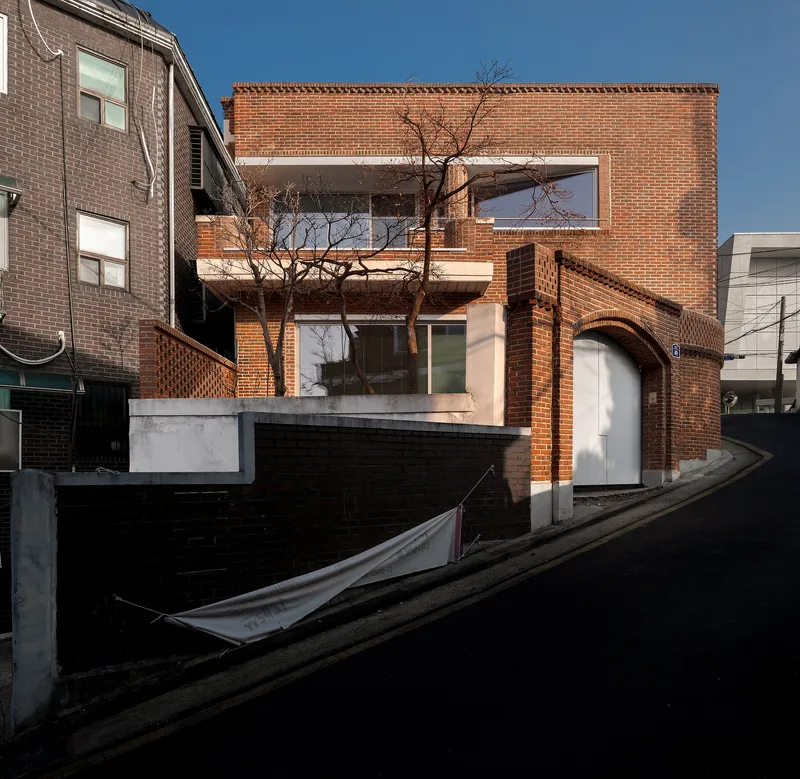 Street view of red brick facade with arched openings and bare tree in late afternoon light