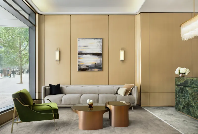 Lobby seating area with beige paneled walls, a corner window overlooking street trees, and copper tables