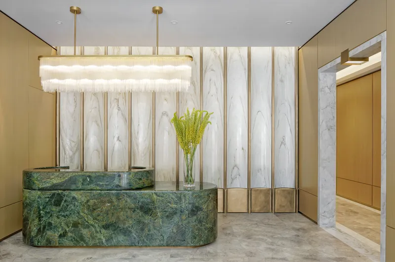 Reception desk clad in green marble with backlit white stone panels and tiered glass chandelier overhead