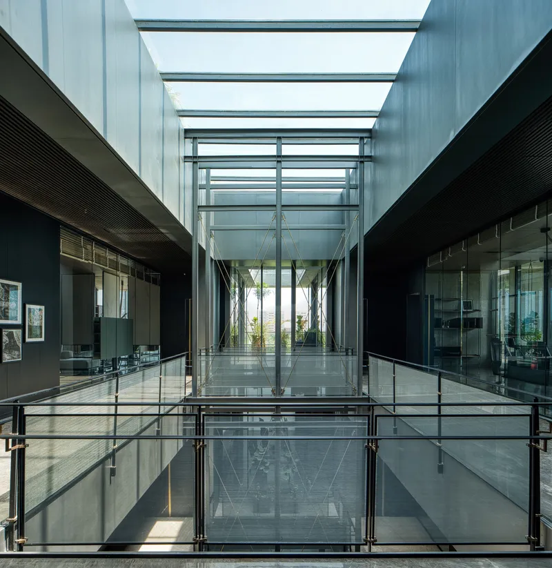 Glass-floored bridge spanning a skylit atrium with steel railings and palm trees visible through glazed walls