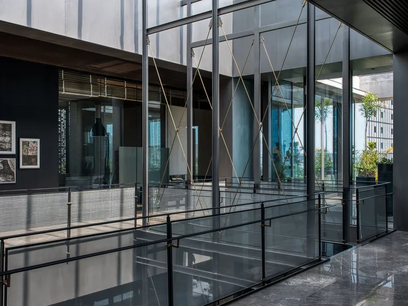 Glass-enclosed atrium with suspended rope bracing and steel walkways connecting interior volumes under overcast skies