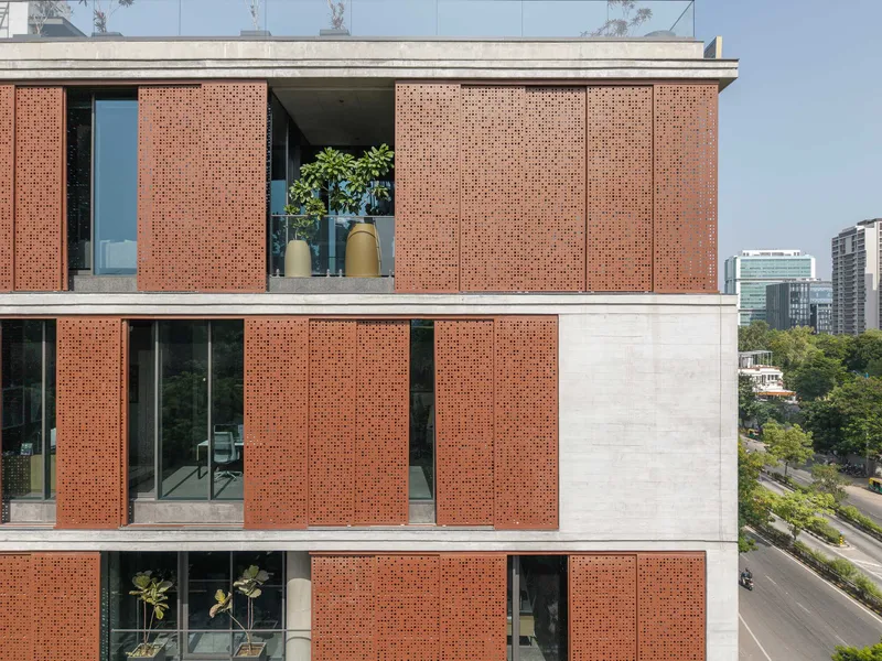 Perforated terracotta panel facade with sliding screens framing balconies and glazed openings under clear blue sky