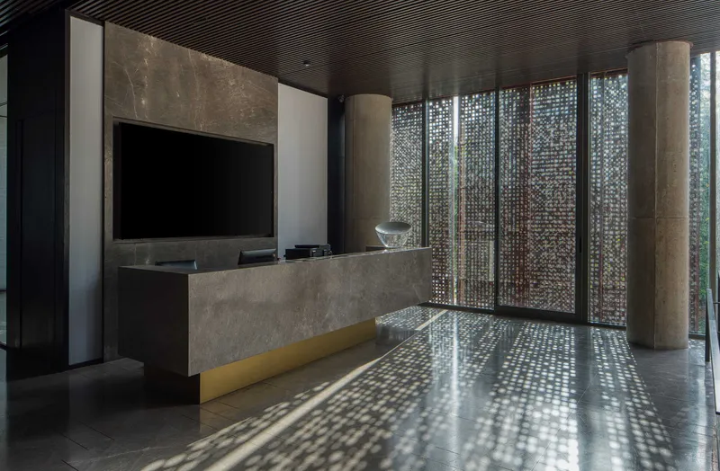 Reception desk with concrete counter and yellow bench beneath black slatted ceiling and filtered daylight