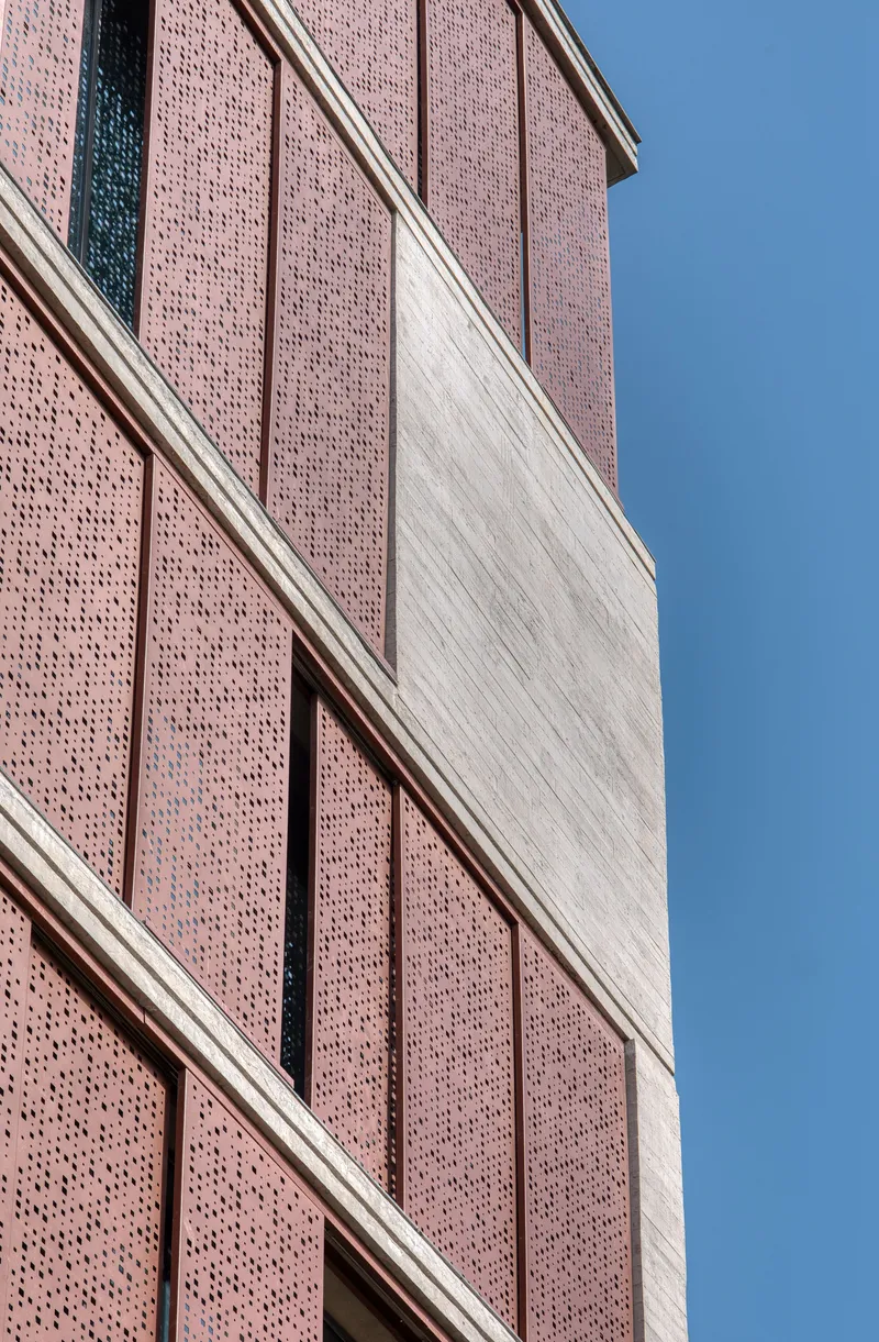 Close-up of perforated brick panels alternating with vertical concrete bands under clear blue sky
