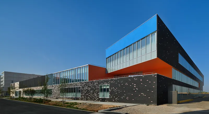 Angled view of the facade showing perforated concrete panels and orange cantilevered volume under blue sky