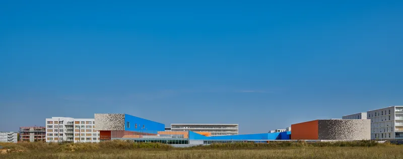 Long elevation view of the horizontal complex with blue and orange volumes across dry grassland