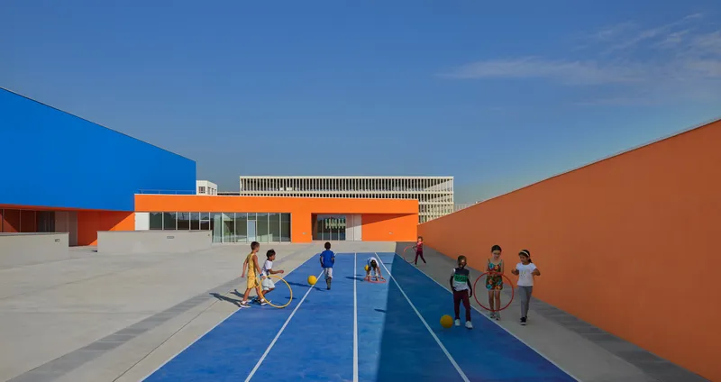 Rooftop courtyard with blue running track surface where children play with hoops in afternoon light