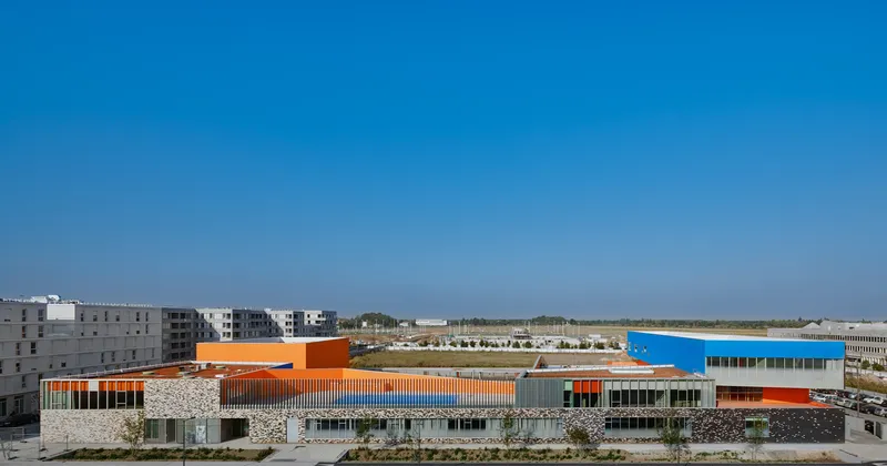 Distant view of the low-slung school building with orange and blue volumes across open terrain